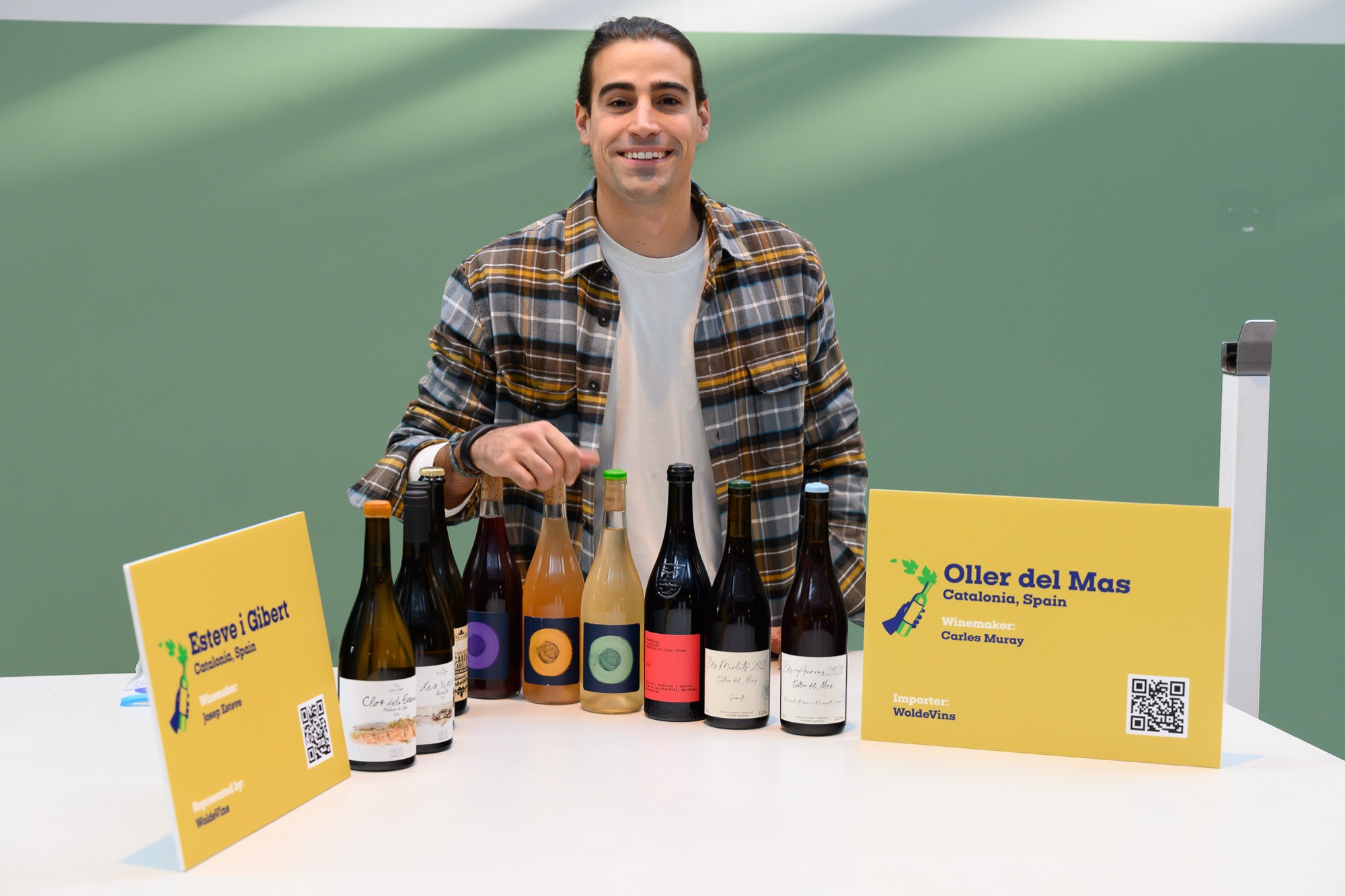 A winemaker behind his tasting table, a row of natural-wine bottles and producer name cards in front of him.
